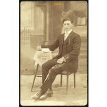 Tóth műterem, Lajosmizse, 1920-as évek, fiú csíkos öltönyben könyvvel, különös (szabadtéri ?) vidéki műterem földes padlóval, festett háttérrel. Eredeti fotó, papírkép.  