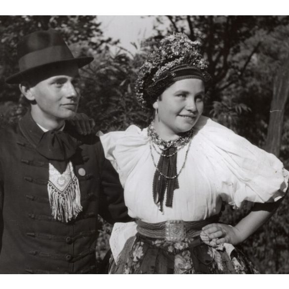 Nagyobb méret, Szendrő István fotóművészeti alkotása, fiatal pár őcsényi népviseletben, Gyöngyösbokréta mozgalom, Őcsény, Tolna megye, népviselet, szoknya, kalap, nyaklánc, fejdísz, 