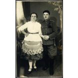 Fiatal pár Dávodról, Kozma műterem, Pécs, magyar katona egyenruhában, bajonettel, tüzérbojttal, sokác (?), bunyevác (?) népviselet, különös harisnya, 2. világháború, 1940-es évek, Eredeti fotó, hátulján feliratozott, pecséttel jelzett papírkép.  