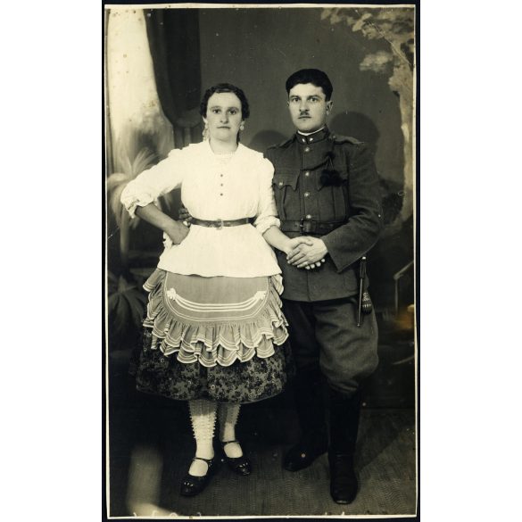 Fiatal pár Dávodról, Kozma műterem, Pécs, magyar katona egyenruhában, bajonettel, tüzérbojttal, sokác (?), bunyevác (?) népviselet, különös harisnya, 2. világháború, 1940-es évek, Eredeti fotó, hátulján feliratozott, pecséttel jelzett papírkép.  