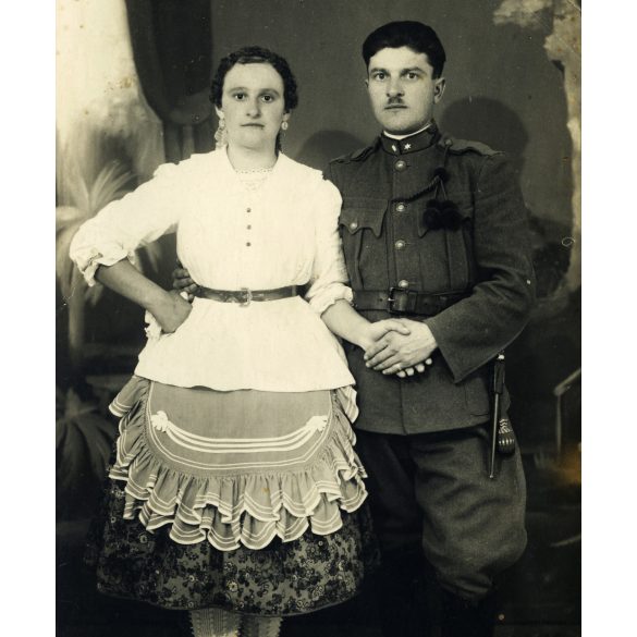 Fiatal pár Dávodról, Kozma műterem, Pécs, magyar katona egyenruhában, bajonettel, tüzérbojttal, sokác (?), bunyevác (?) népviselet, különös harisnya, 2. világháború, 1940-es évek, Eredeti fotó, hátulján feliratozott, pecséttel jelzett papírkép.  