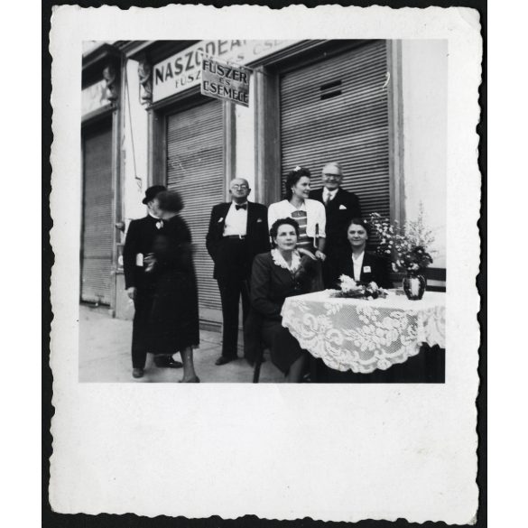 Elegáns nők és férfiak a fűszer-csemege bolt előtt, Beszterce, Erdély, magyar feliratok, 2. világháború, Naszódean György üzlete, Szászsebes utca 7., üzlet, kirakat, Horthy-korszak , 1940-es évek. Eredeti fotó, papírkép.   méret megközelítőleg (centi